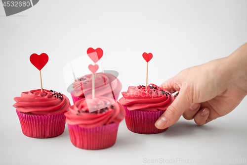 Image of close up of hand taking cupcakes with heart sticks