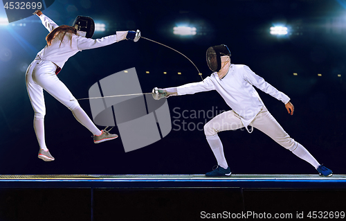 Image of Two fencing athletes fight on professional sports arena