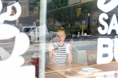 Image of Thoughtful woman reading news on mobile phone during rest in coffee shop.