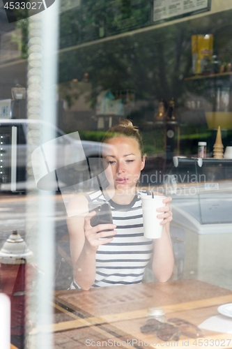 Image of Thoughtful woman reading news on mobile phone during rest in coffee shop.