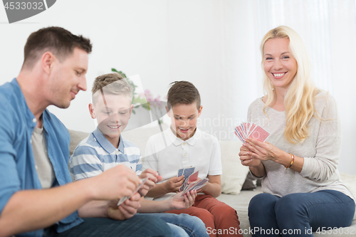 Image of Happy young family playing card game at home.