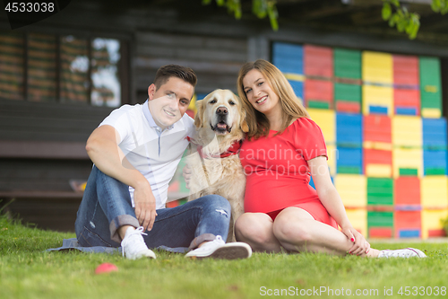 Image of A Young couple expecting baby with their Golden retriever dog