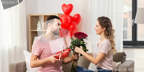 Image of happy man giving woman flowers and present at home