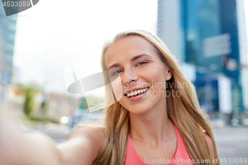 Image of happy young woman taking selfie on city street