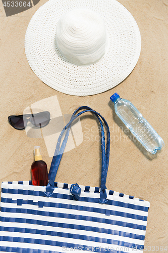 Image of beach bag, sunscreen, sunglasses and hat on sand