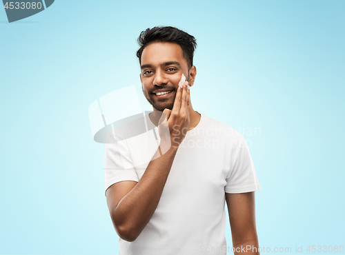 Image of happy indian man applying cream to face