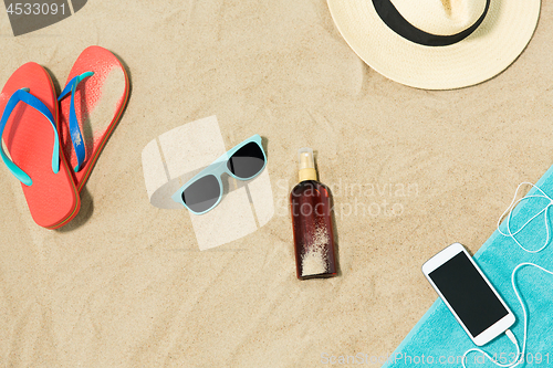 Image of smartphone, hat, flip flops and shades on beach
