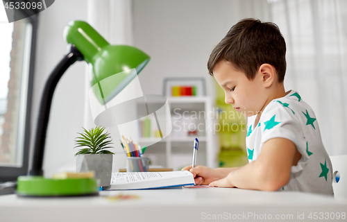 Image of student boy with book writing to notebook at home