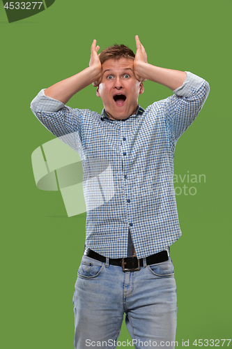 Image of The young attractive man looking suprised isolated on green