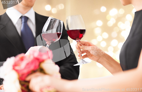 Image of hands of couple clinking red wine glasses