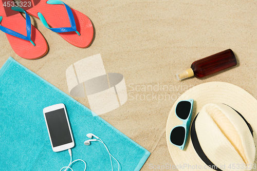 Image of smartphone, hat, flip flops and shades on beach