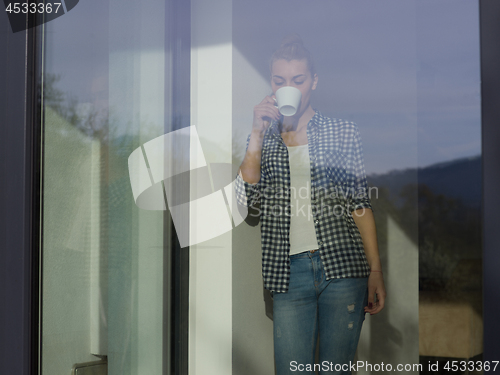 Image of young woman drinking morning coffee by the window