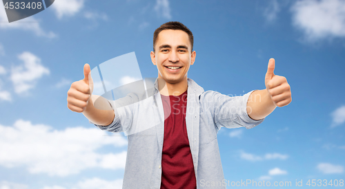 Image of happy young man showing thumbs up over blue sky
