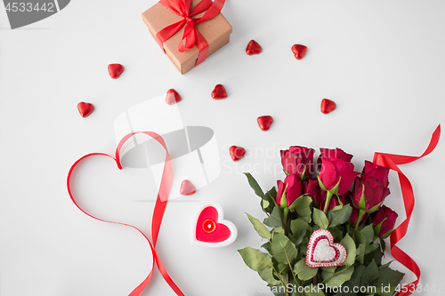 Image of close up of red roses, gift, candies and candle