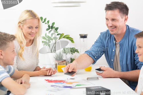 Image of Happy young family playing card game at dining table at bright modern home.