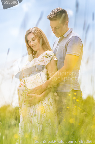 Image of Young happy pregnant couple hugging in nature.