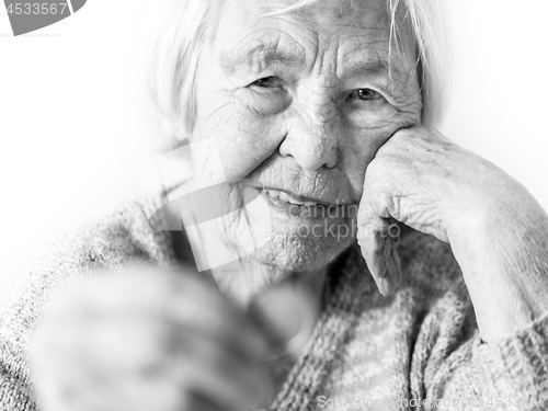 Image of Cheerful elderly 96 years old woman sitting at table at home happy with a coin in her hand. Saving for retirement and financial planing concept in black and white.
