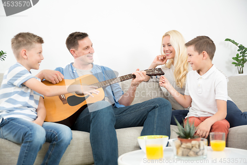 Image of Happy caucasian family smiling, playing guitar and singing songs together at cosy modern home