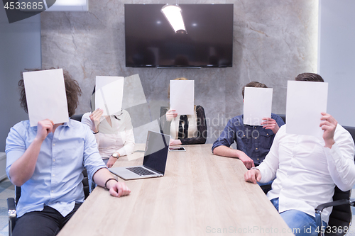 Image of startup business team holding a white paper over face