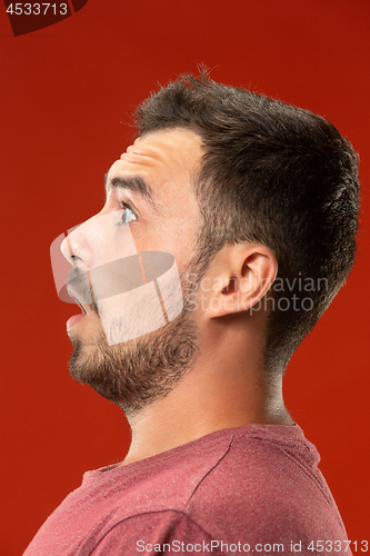 Image of The young attractive man looking suprised isolated on red