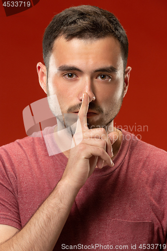 Image of The young man whispering a secret behind her hand over red background