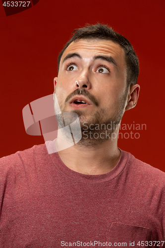 Image of The young attractive man looking suprised isolated on red