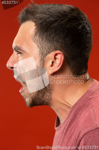 Image of The young emotional angry man screaming on red studio background