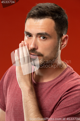 Image of The young man whispering a secret behind her hand over red background