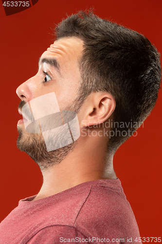 Image of The young attractive man looking suprised isolated on red