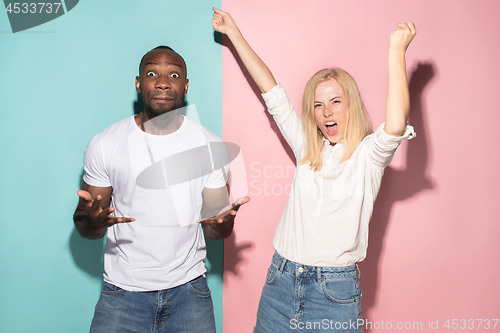 Image of We won. Winning success happy afro man and woman celebrating being a winner. Dynamic image of caucasian female and male model on pink studio.