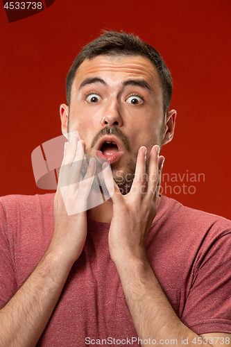 Image of The young attractive man looking suprised isolated on red