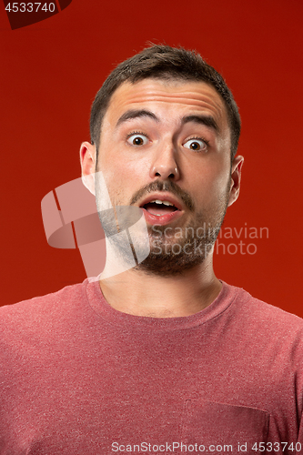 Image of The young attractive man looking suprised isolated on red