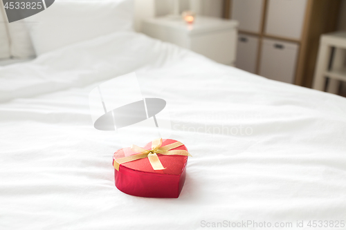 Image of red gift box in shape of heart on bed at home