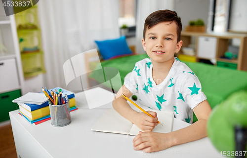 Image of happy boy writing or drawing to notebook at home