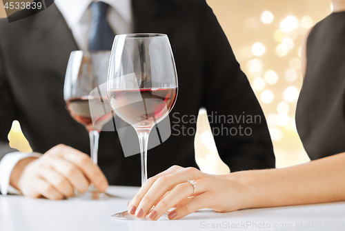 Image of hands of engaged couple with red wine in glasses