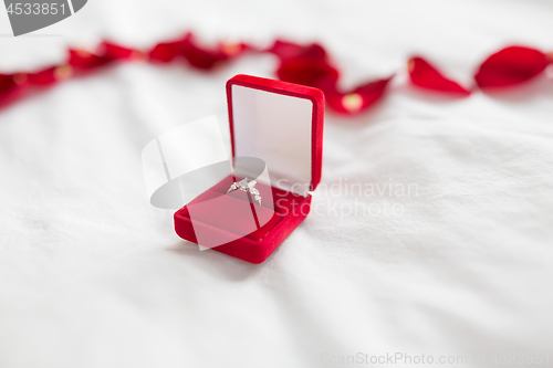 Image of diamond ring in red velvet gift box on bed sheet