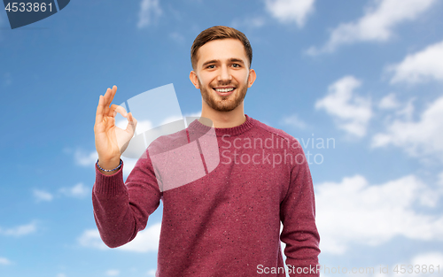 Image of smiling man showing ok hand sign over blue sky