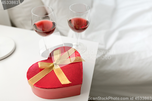 Image of gift and two glasses of wine in bedroom at home