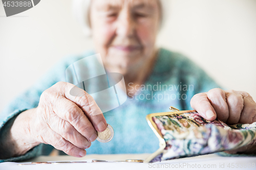 Image of Concerned elderly woman sitting at the table counting money in her wallet.