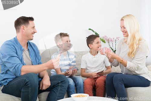 Image of Happy young family playing card game at home.