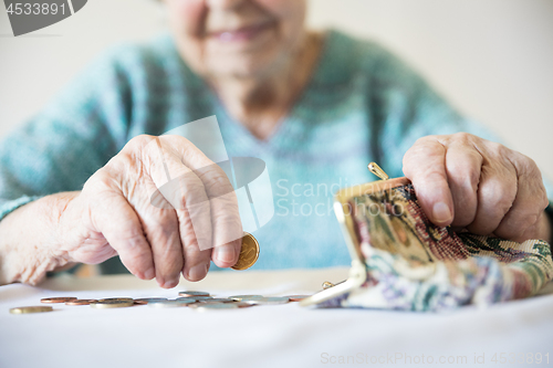 Image of Detailed closeup photo of unrecognizable elderly womans hands counting remaining coins from pension in her wallet after paying bills.