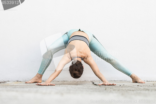 Image of Fit sporty active girl in fashion sportswear doing yoga fitness exercise in front of gray wall, outdoor sports, urban style