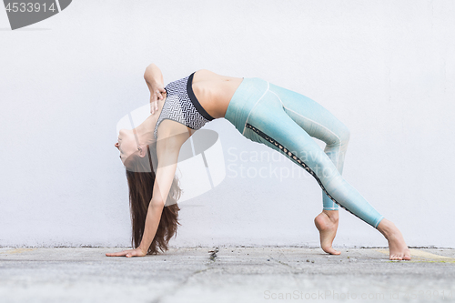 Image of Fit sporty active girl in fashion sportswear doing yoga fitness exercise in front of gray wall, outdoor sports, urban style