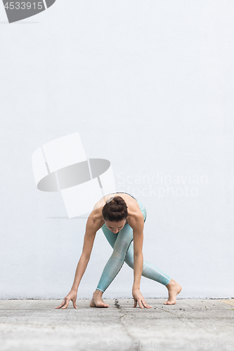 Image of Fit sporty active girl in fashion sportswear doing yoga fitness exercise in front of gray wall, outdoor sports, urban style