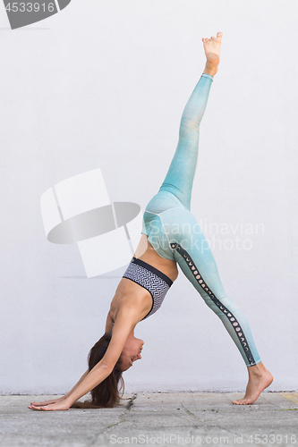 Image of Fit sporty active girl in fashion sportswear doing yoga fitness exercise in front of gray wall, outdoor sports, urban style