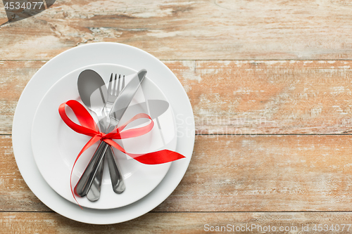 Image of cutlery tied with red ribbon on set of plates