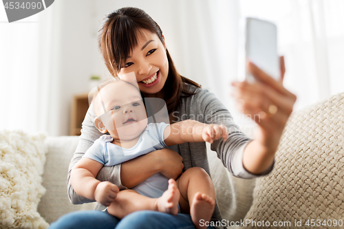Image of happy mother with baby son taking selfie at home