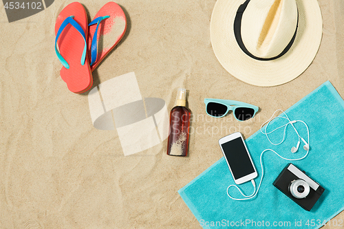 Image of smartphone, hat, flip flops and shades on beach