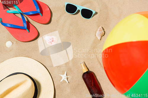 Image of hat, flip flops and shades and beach ball on sand