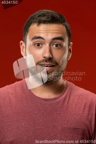 Image of The young attractive man looking suprised isolated on red